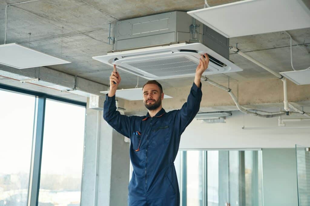 A man repairs the ventilation system, the device hangs on the ceiling