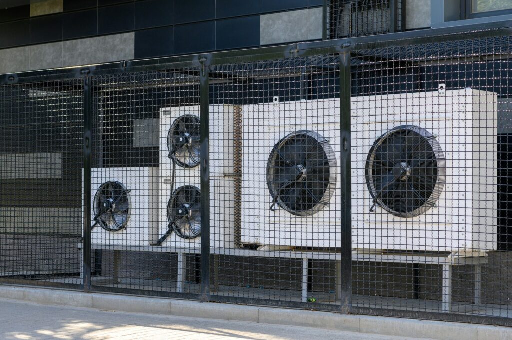 Air conditioning compressor system on a modern building protected by a metal fence.